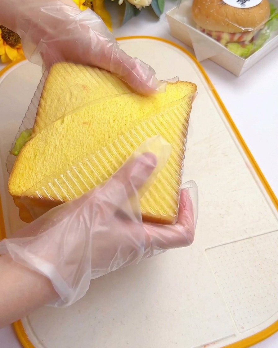 Mani che premono il sandwich alto in uno stampo di plastica triangolare trasparente su un tagliere.