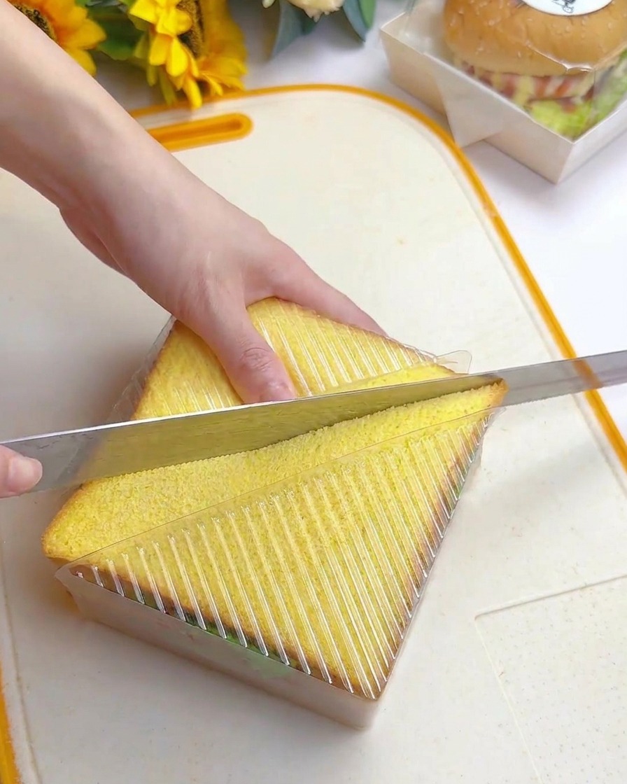 Una mano che usa un lungo coltello seghettato per tagliare in diagonale il sandwich dentro lo stampo.