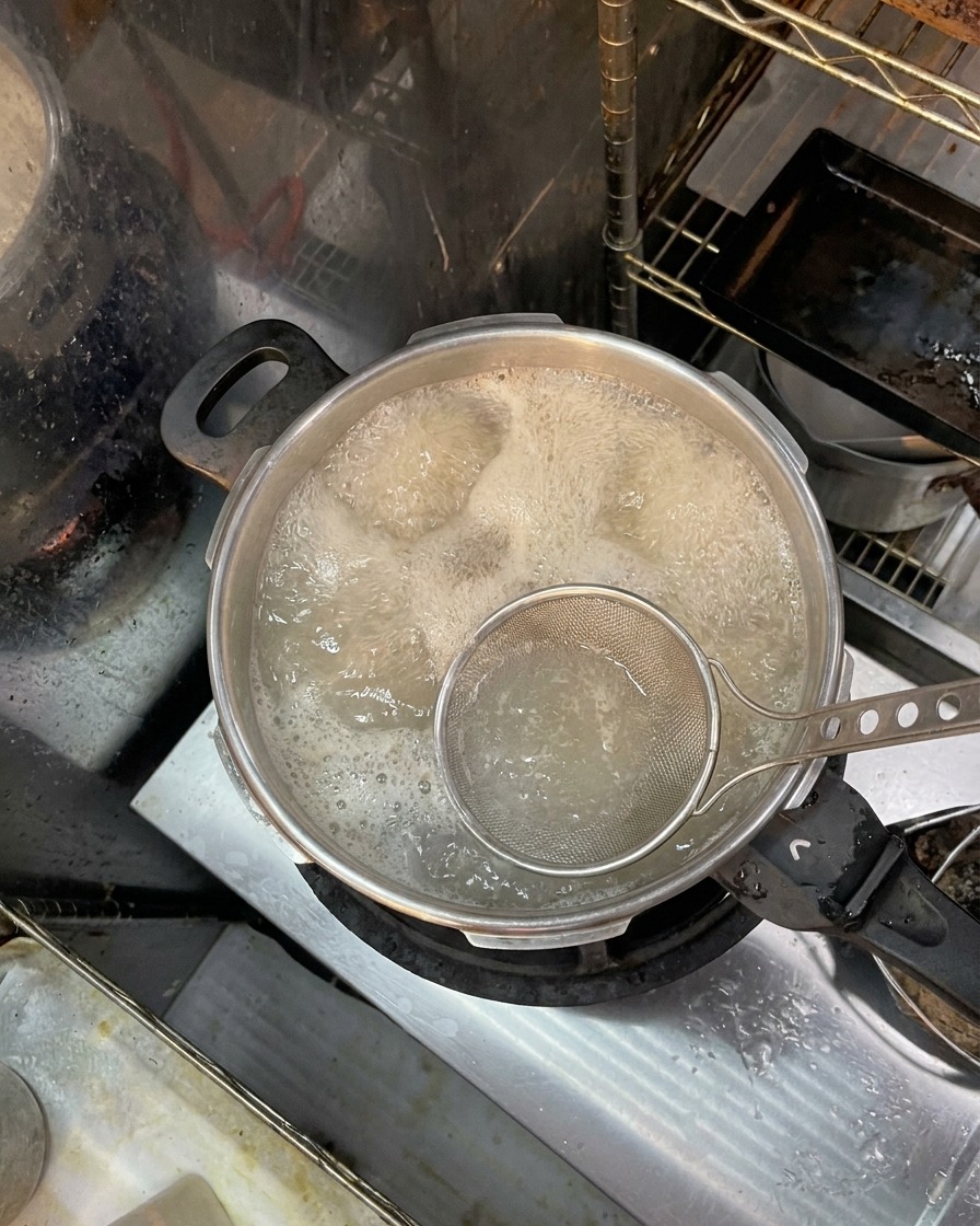 Una schiumarola a maglia fine che rimuove schiuma marroncina e impurità dalla superficie dellacqua bollente con le ossa.