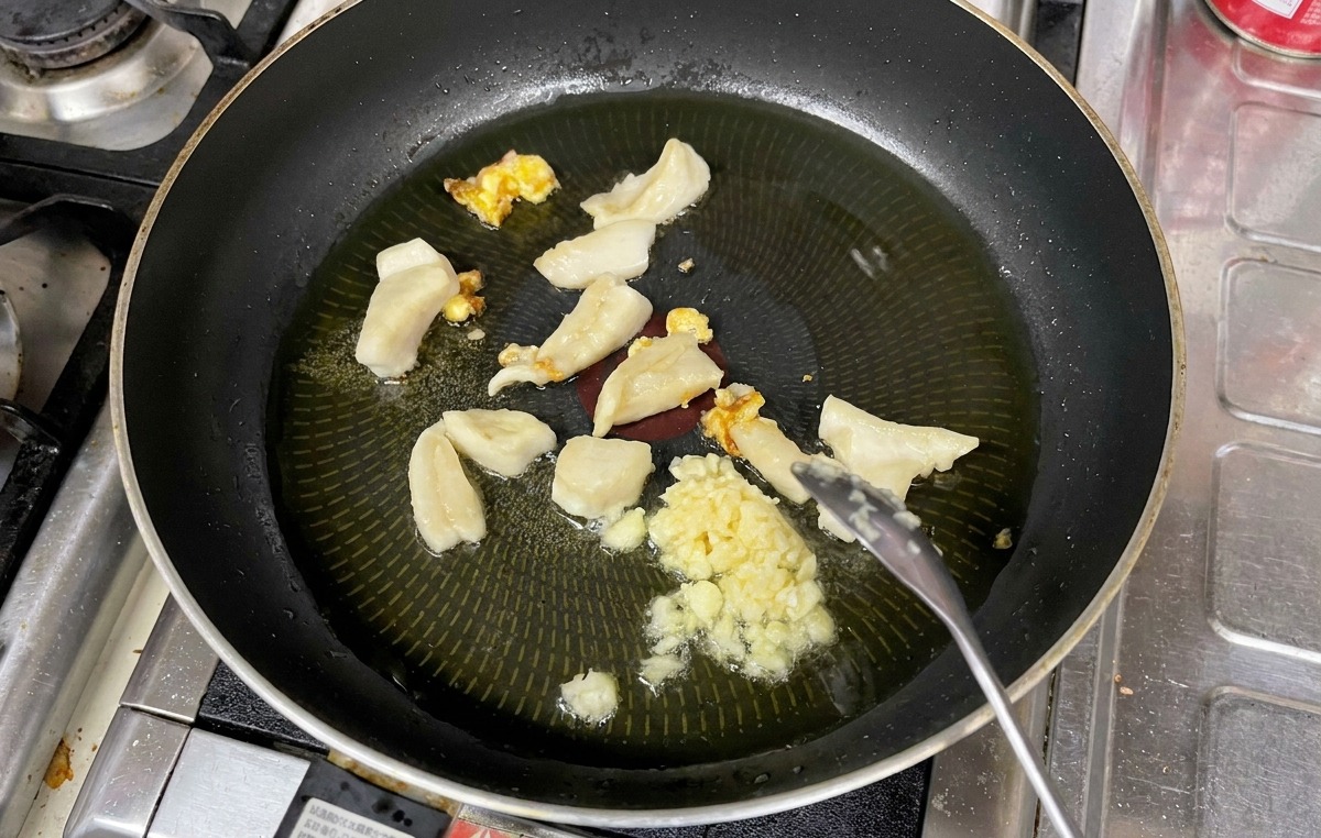Aglio tritato mescolato con un cucchiaio insieme a pezzi di grasso fuso in una padella con olio caldo.
