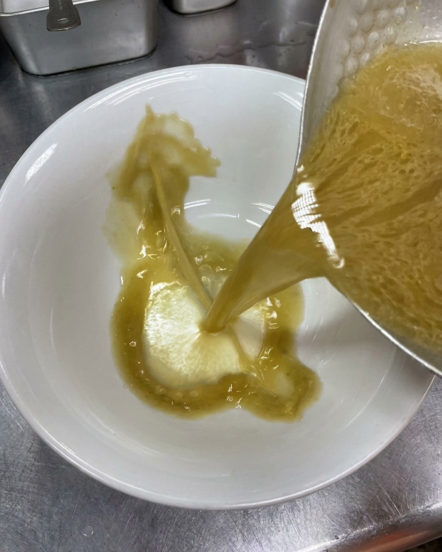 Brodo tonkotsu condito e opaco versato da una pentola di metallo in una ciotola di ceramica bianca pulita.