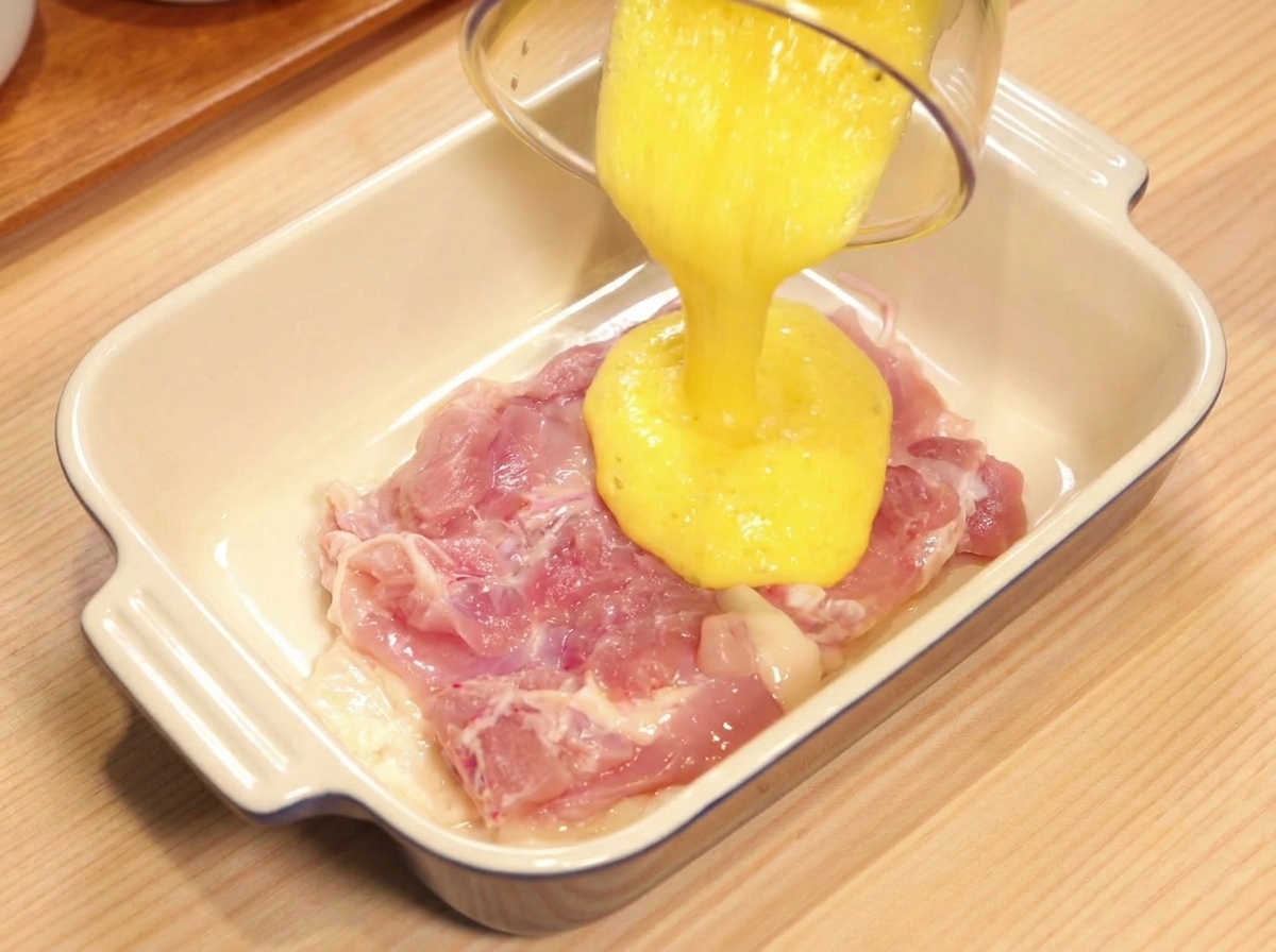 Succo di ananas giallo versato da un contenitore su una sovracoscia di pollo cruda in un piatto di ceramica.