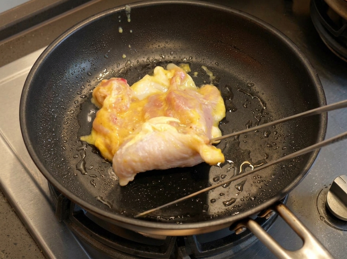 Sovracoscia di pollo cruda adagiata in una padella calda con olio usando delle pinze.