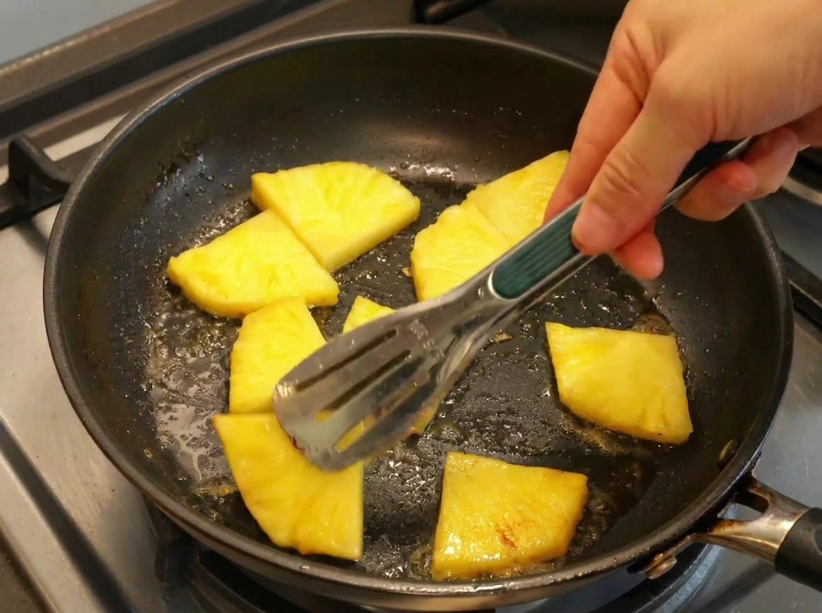 Pinze che girano fette di ananas giallo in una padella calda con burro.