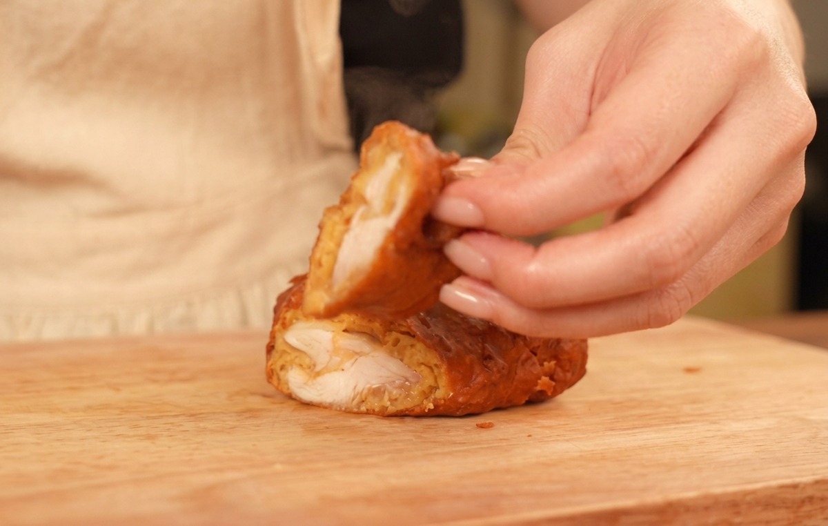 Dita che mostrano un pezzo di pollo fritto tagliato a metà, rivelando la crosta dorata e linterno succoso.