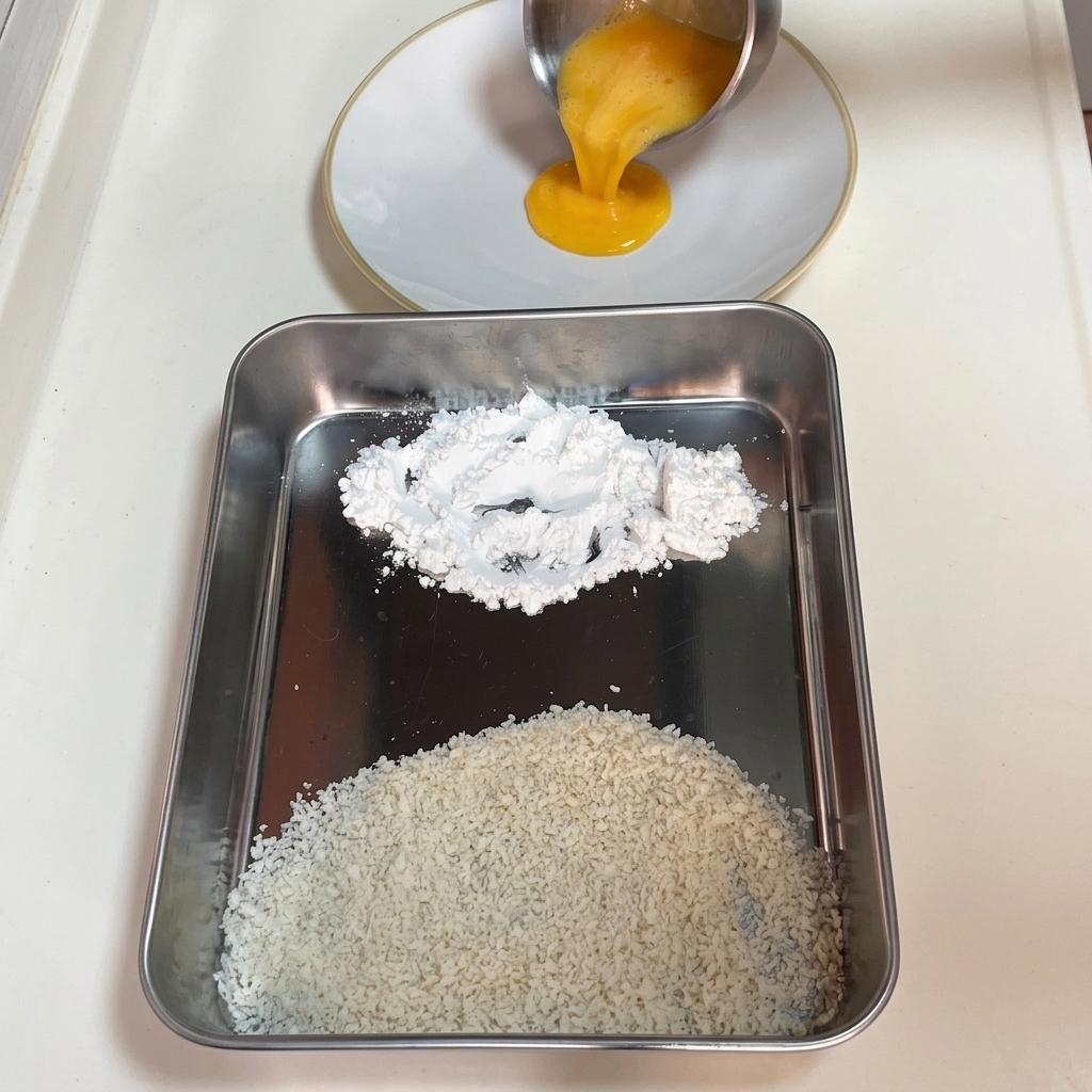 Uovo sbattuto versato in un piatto bianco accanto a un vassoio con amido di mais e panko.