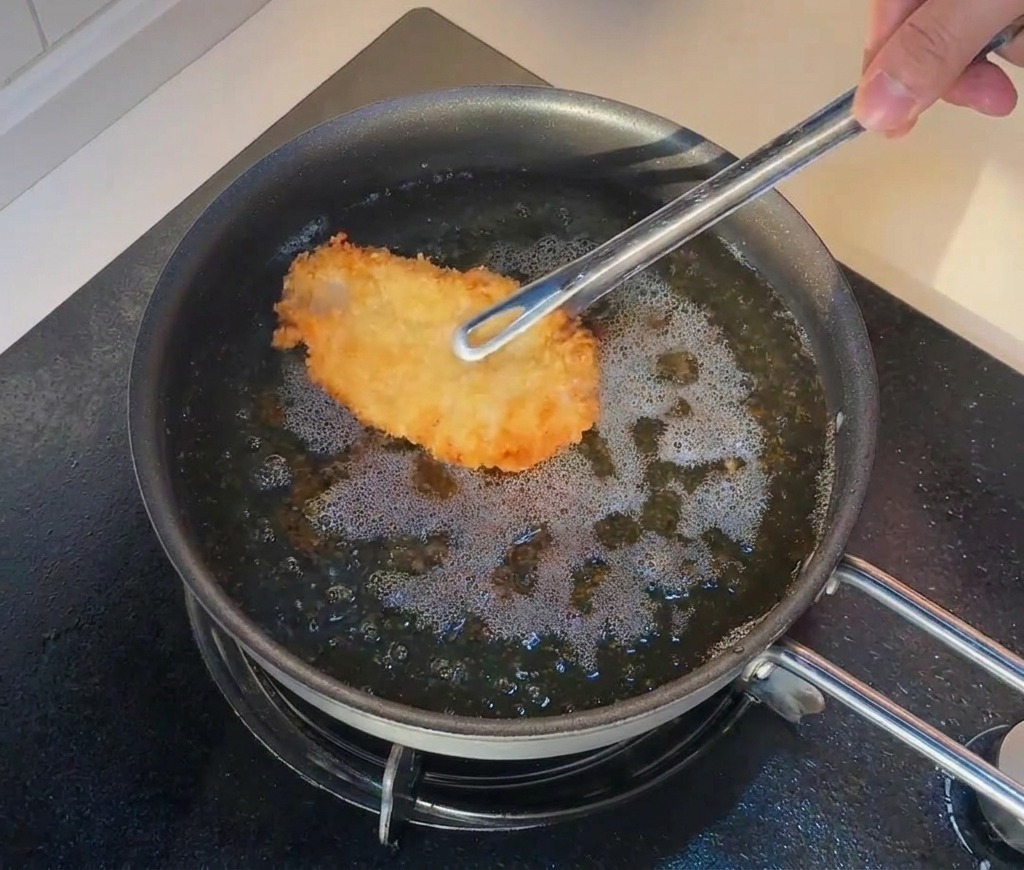 Pinze che rimettono il pollo già fritto nellolio molto caldo per una seconda frittura.