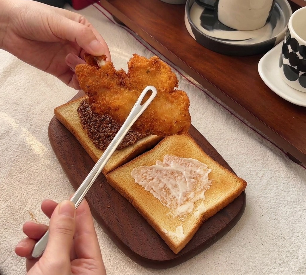 Pinze che appoggiano un grande filetto di pollo croccante sulla fetta di pane con la senape.