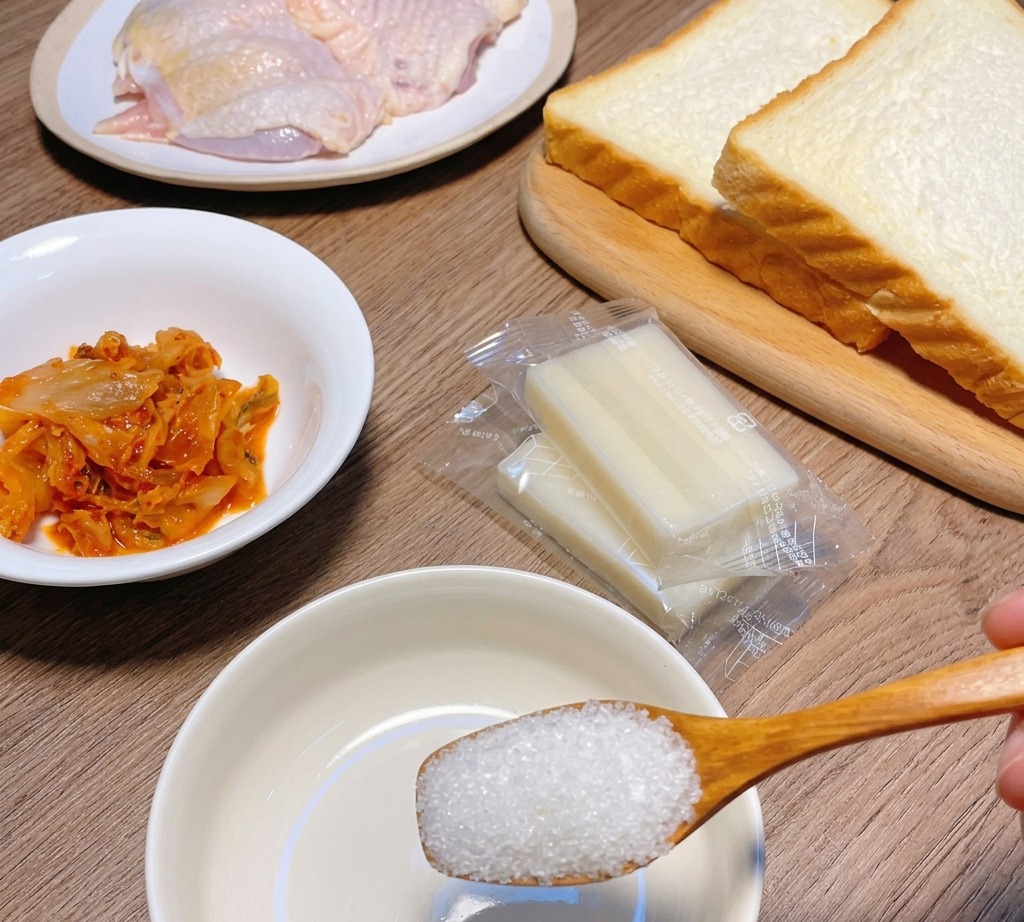 Un cucchiaio di legno con zucchero sopra una ciotolina bianca circondata da ingredienti per il sandwich.