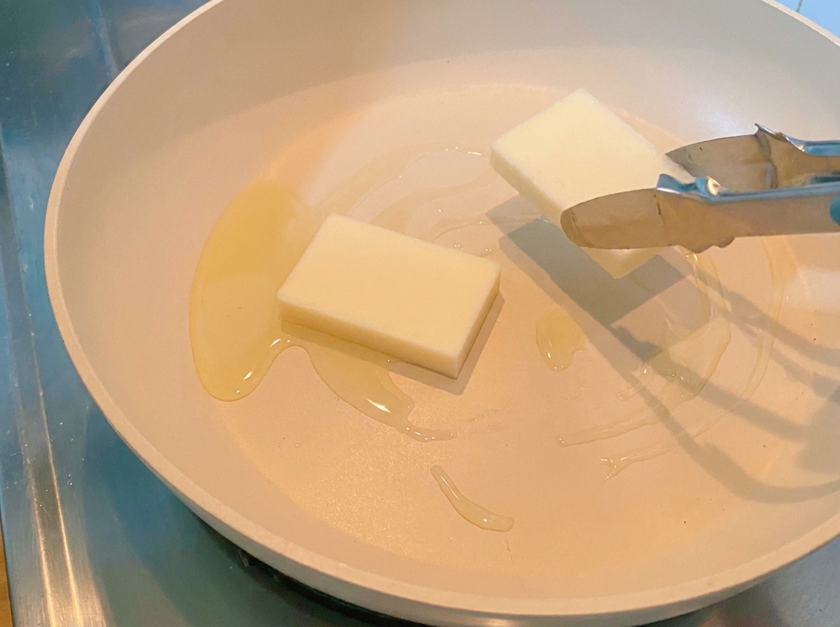 Pinze che posizionano due torte di riso bianco spesse in una padella calda.