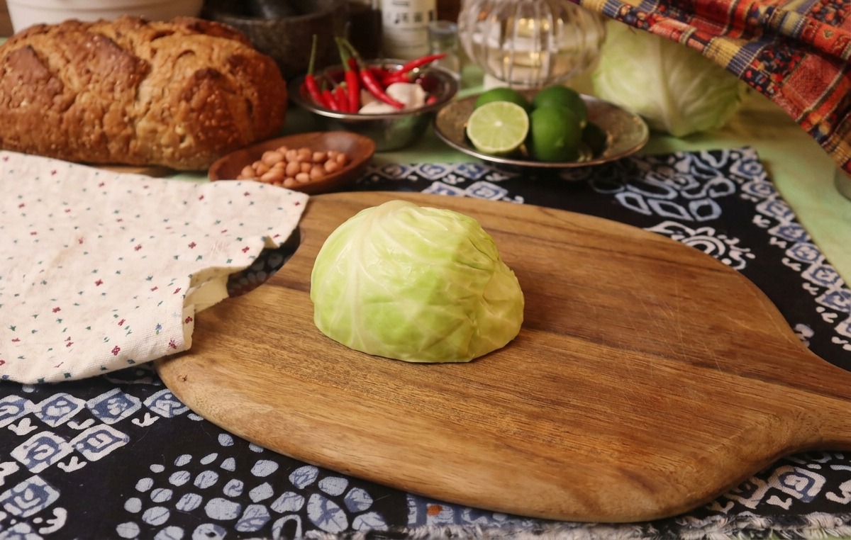 Un quarto di cavolo verde fresco su un tagliere di legno accanto a un panno decorato.
