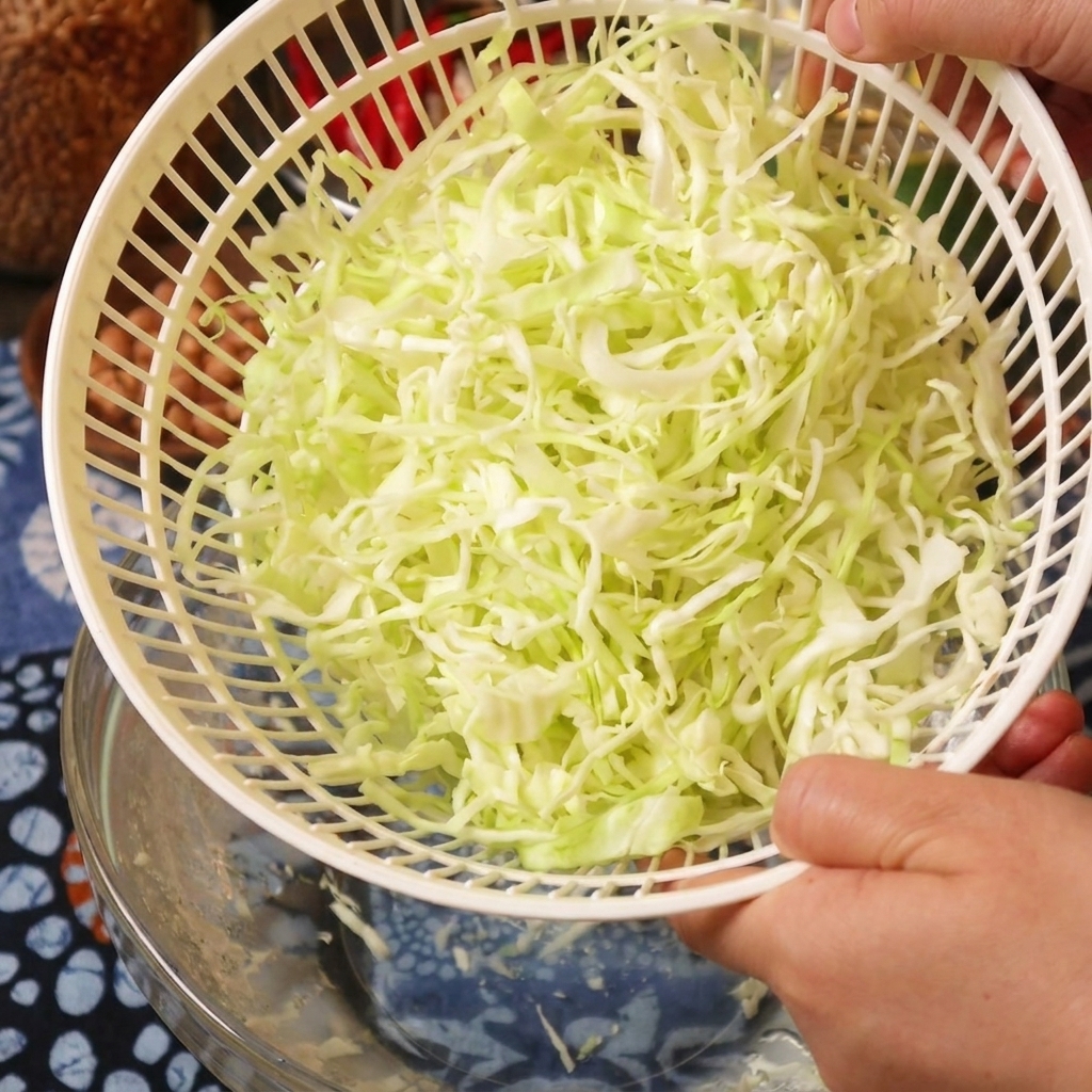 Una persona che tiene il cestello di una centrifuga per insalata pieno di cavolo appena asciugato.