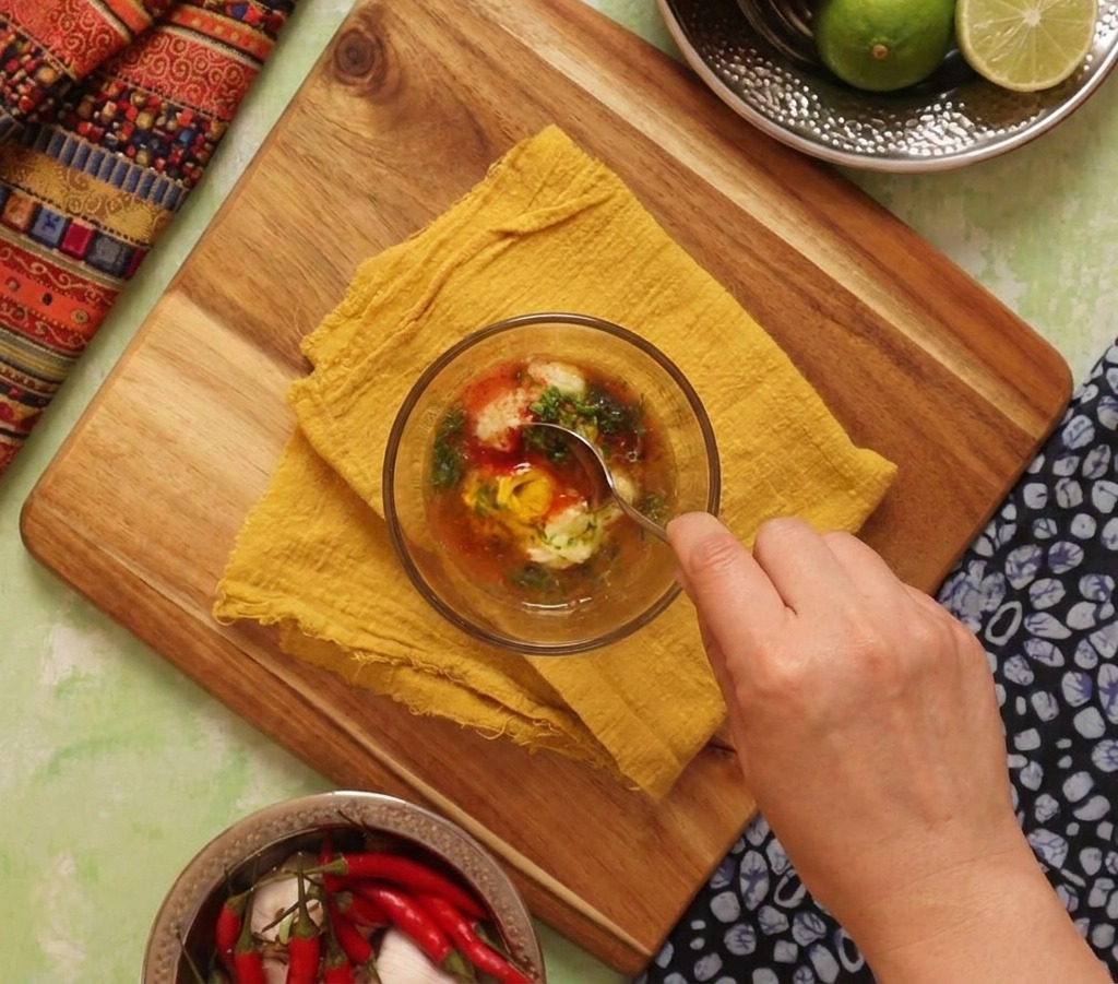 Mano che mescola una salsa cremosa arancione fatta di maionese, lime e spezie con un cucchiaio.