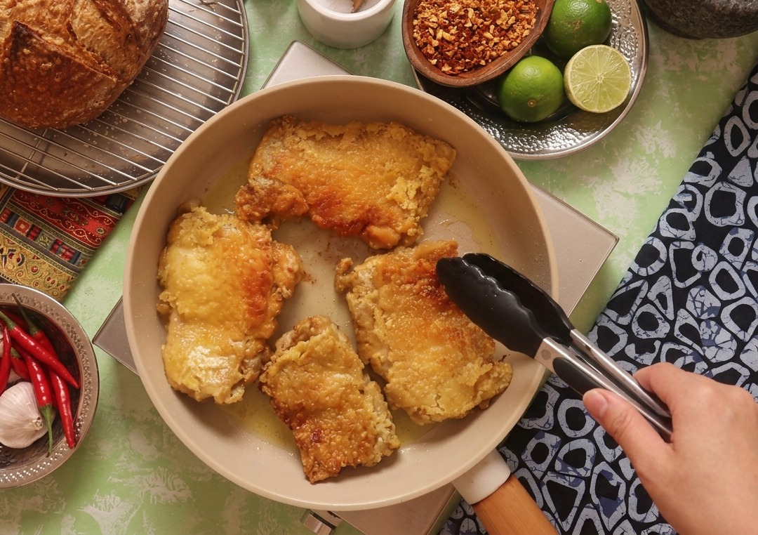 Pinze da cucina nere che girano un pezzo di pollo mostrando una superficie perfettamente dorata e croccante.