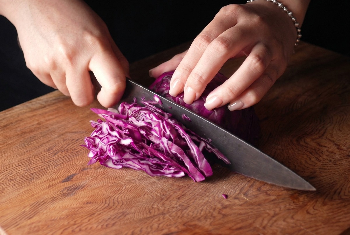 Una persona che affetta finemente un cavolo viola con un coltello da chef su un tagliere di legno.