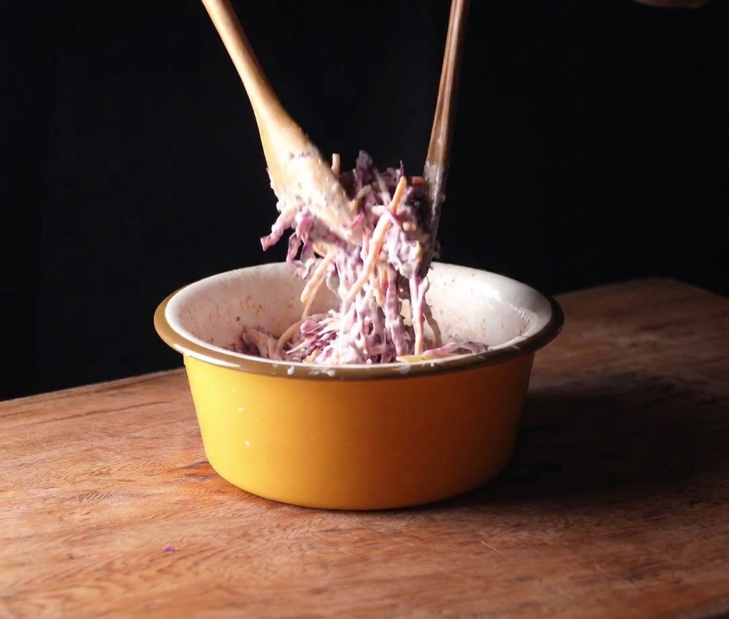 Cavolo viola e carote mescolati con una salsa cremosa in una ciotola gialla usando cucchiai di legno.