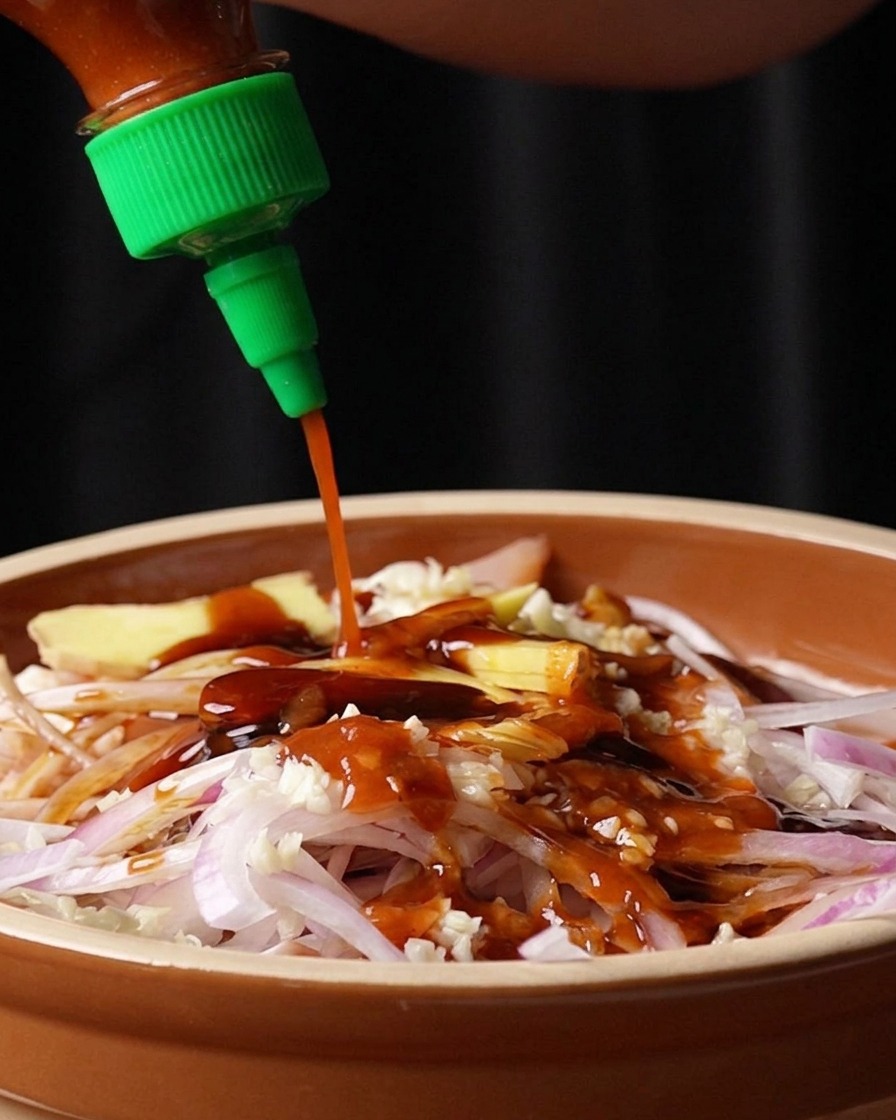 Salsa piccante Sriracha versata da una bottiglia sopra il pollo e gli aromi.