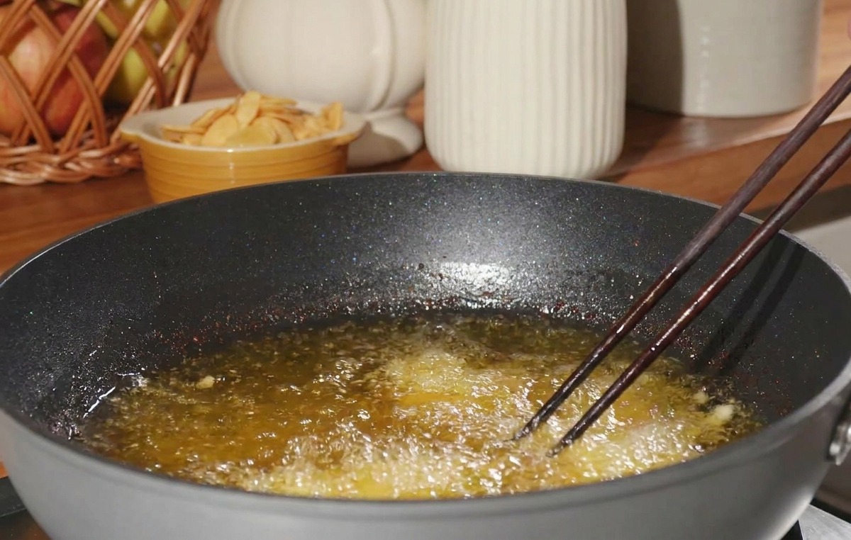 Pezzo di pollo infarinato immerso in olio bollente usando le bacchette.