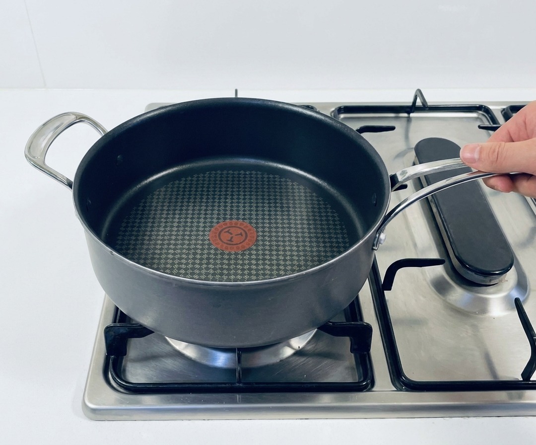 Una padella antiaderente su un fornello a gas con la fiamma accesa.