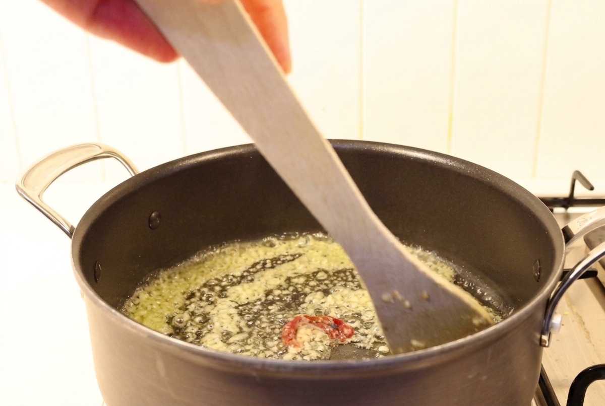 Aglio tritato e peperoncino mescolati al burro fuso in una pentola con una spatola di legno.