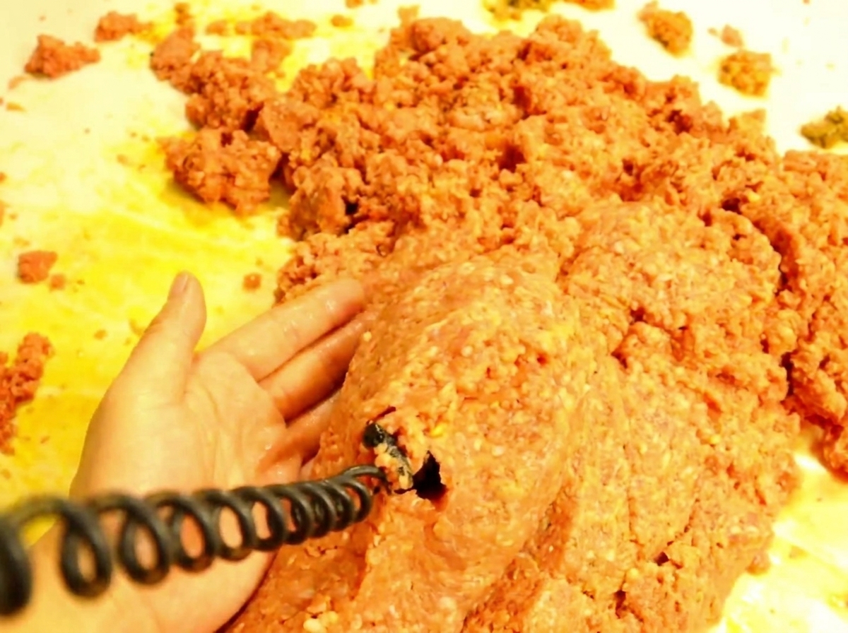 Cucchiaio di legno che versa la carne succosa su metà panino tostato.