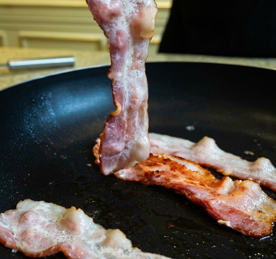 Sollevare una fetta di pancetta parzialmente cotta e dorata in padella usando delle pinze da cucina.