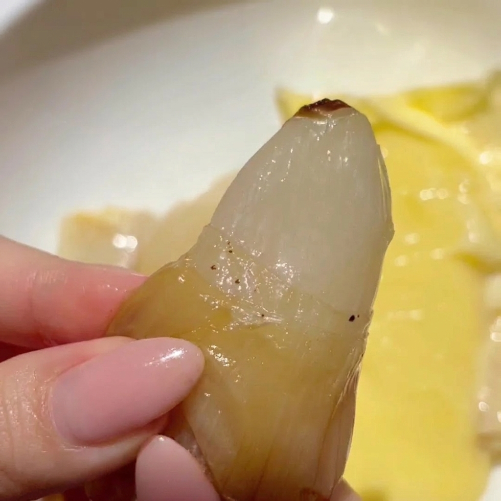 Una mano che schiaccia un singolo spicchio daglio arrosto, dorato e traslucido, per farlo uscire dalla sua buccia cartacea.