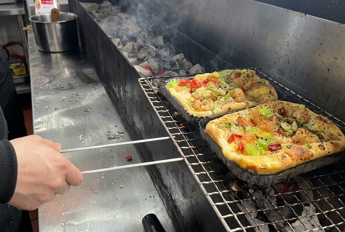 Una pizza rettangolare con gamberi e verdure miste viene posizionata sulla griglia di un barbecue a carbone.