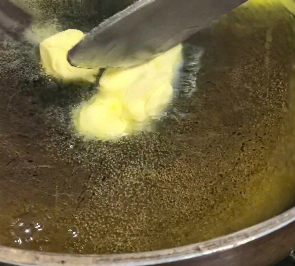 Cubetti di burro che si sciolgono e sfrigolano in una padella scura a fuoco basso.