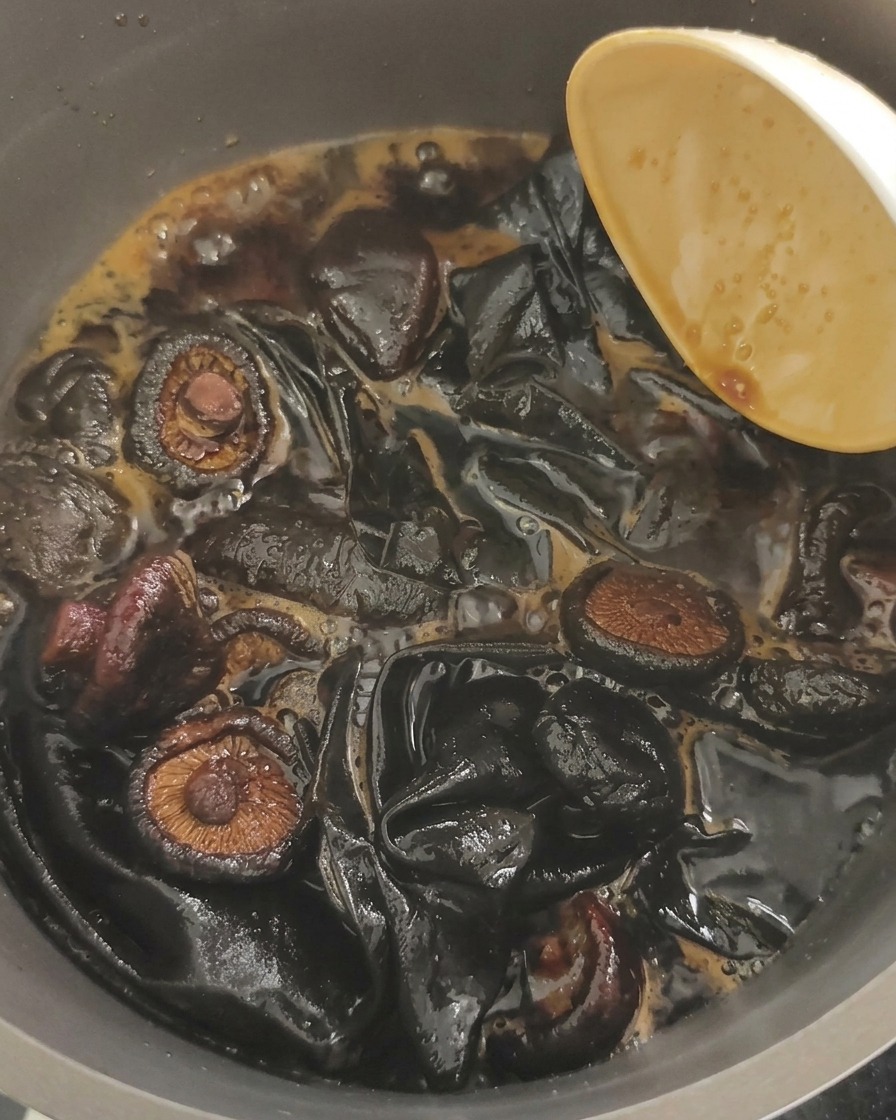 Primo piano di funghi orecchio di Giuda e grandi pezzi di alga kombu che sobbollono in un liquido di soia scuro.