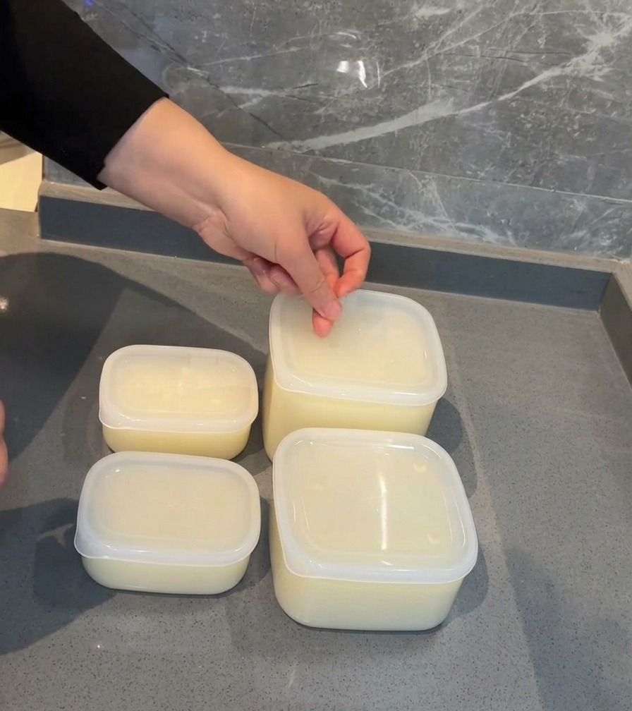 Una mano applica unetichetta bianca con la data sul coperchio di un contenitore di plastica trasparente pieno di brodo di maiale.