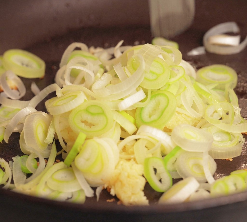Maiale macinato crudo, aglio tritato e un mucchietto di cipollotto affettato in una padella scura pronti per essere cotti.
