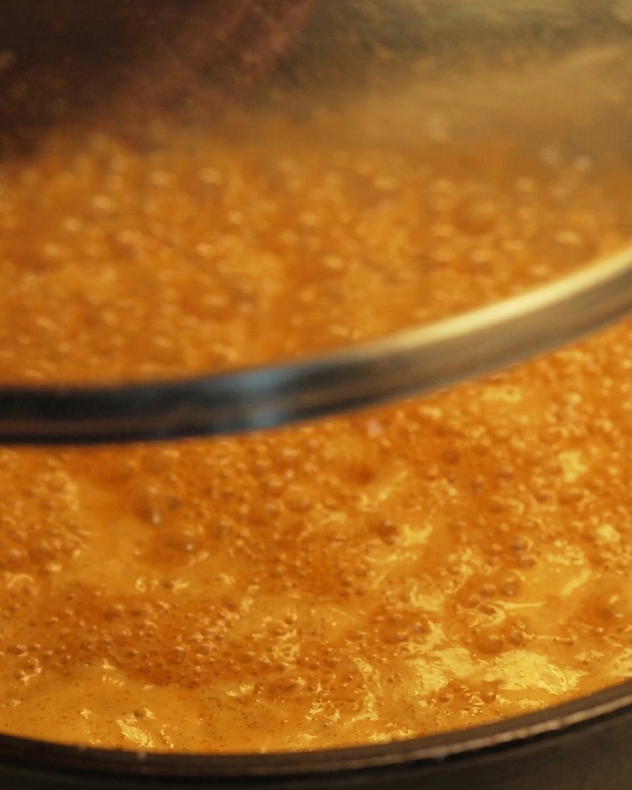 Un coperchio di vetro trasparente che viene abbassato su una padella contenente una salsa arancione che sobbolle dolcemente.