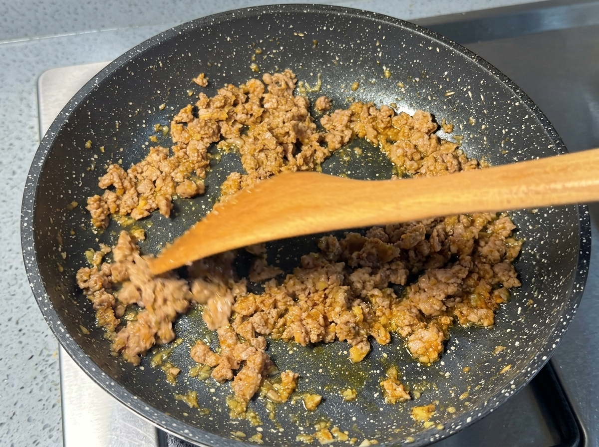 Carne di maiale macinata e rosolata saltata in padella con una spatola di legno.
