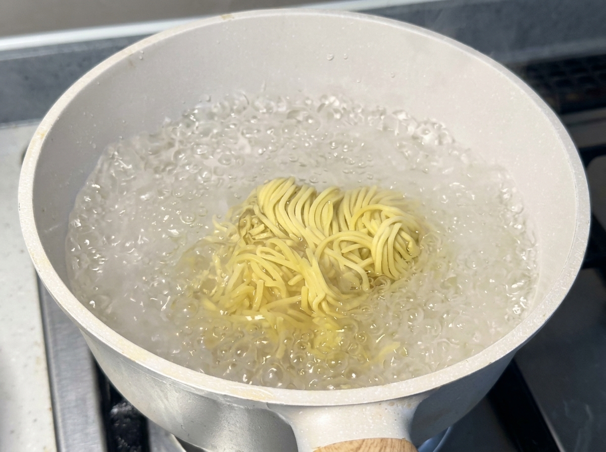 Un nido di noodles ramen gialli e freschi che bolle vigorosamente in una pentola bianca colma dacqua.
