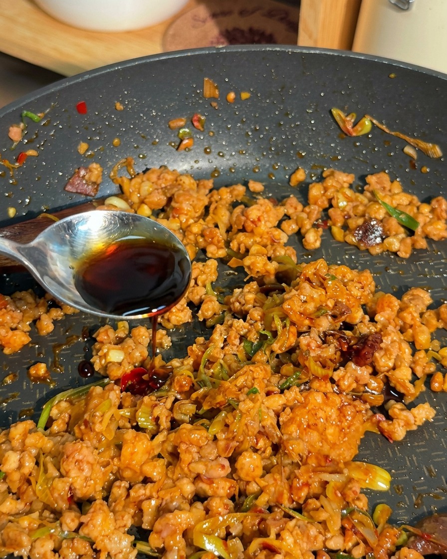 Un liquido scuro e saporito viene versato da un cucchiaio dargento sopra il mix di carne macinata e cipollotti.