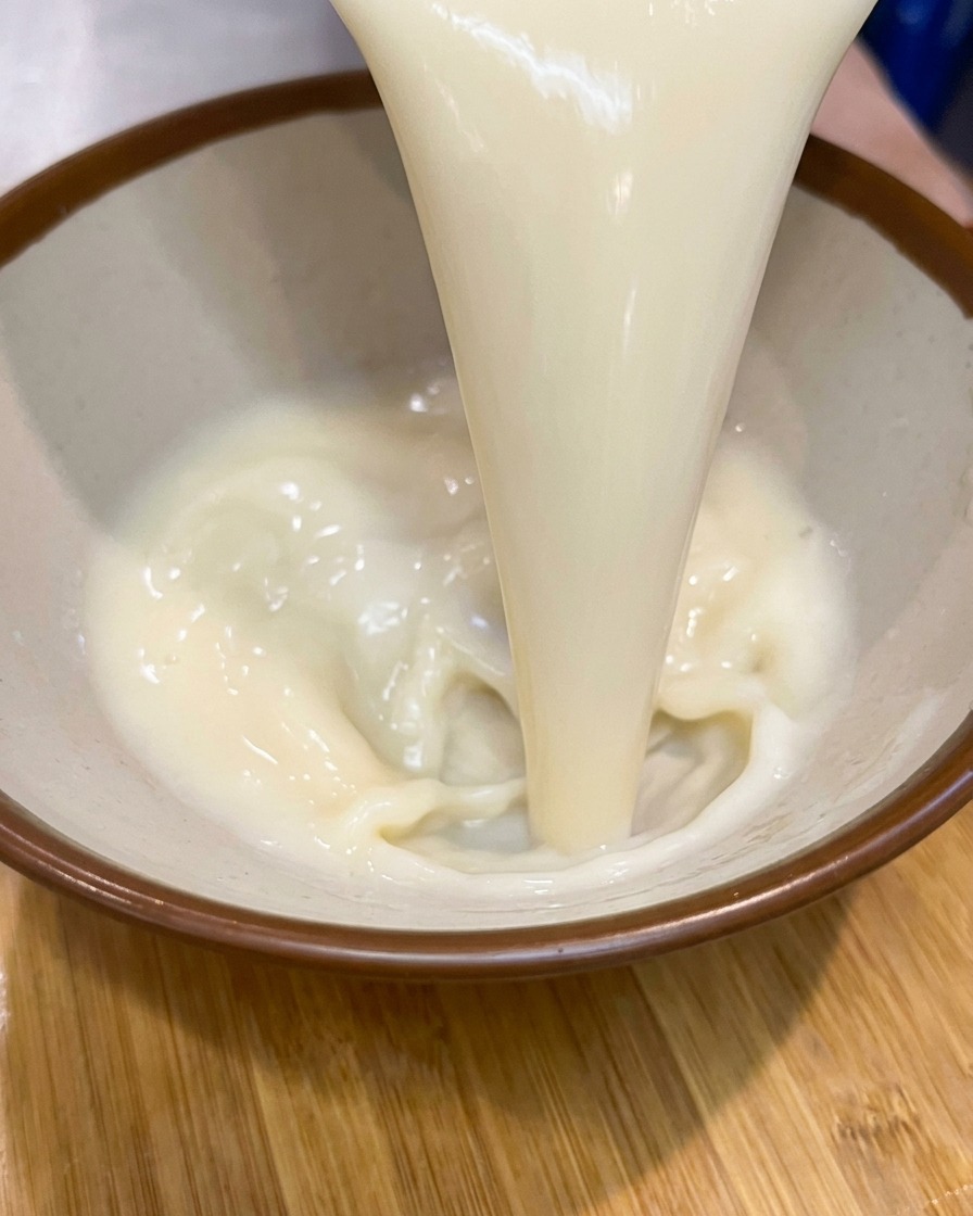 Un flusso denso di base per zuppa chiara e cremosa versato in una ciotola di ceramica con il bordo marrone.