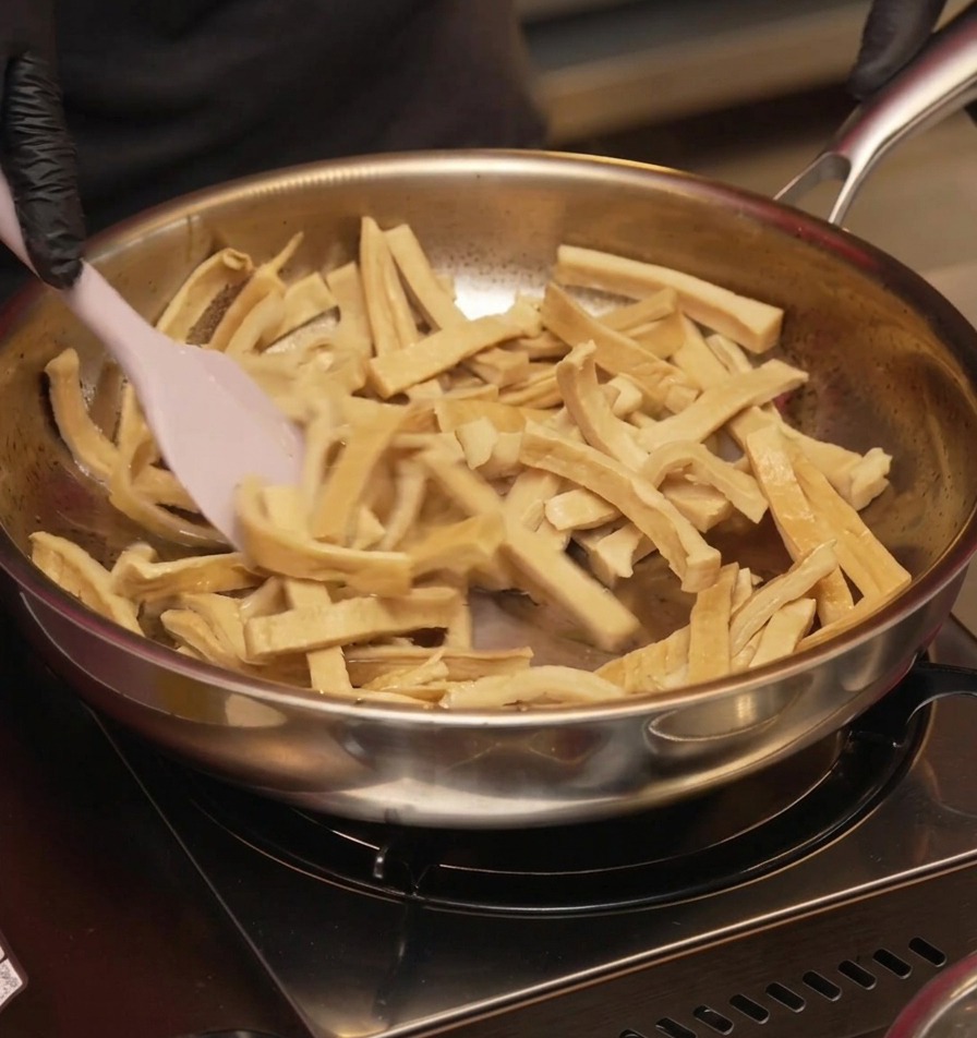 Germogli di bambù a fette saltati in padella con una spatola di silicone rosa fino ad apparire asciutti e leggermente dorati.