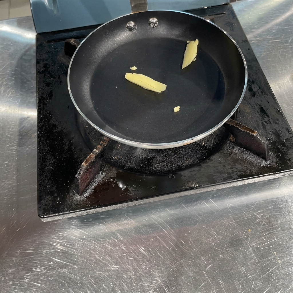 Un piccolo pezzetto di burro giallo che si scioglie allinterno di una padella nera a fondo piatto sul fornello.