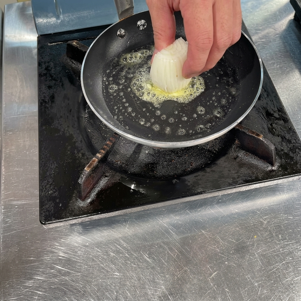 Una mano che mette una manciata di cipolle bianche affettate in una padella calda con burro fuso spumeggiante.