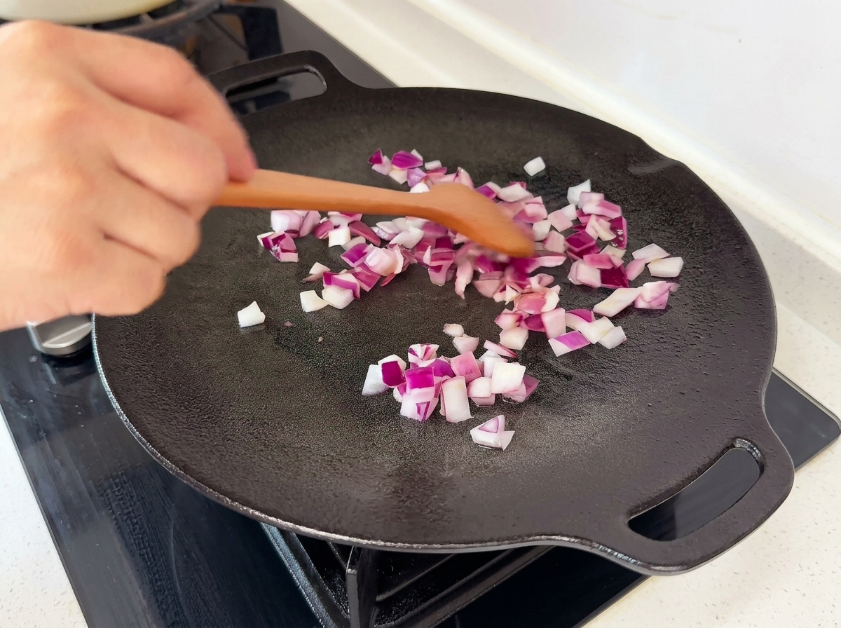 Cipolle rosse a cubetti saltate in una padella piatta nera con una spatola di legno.