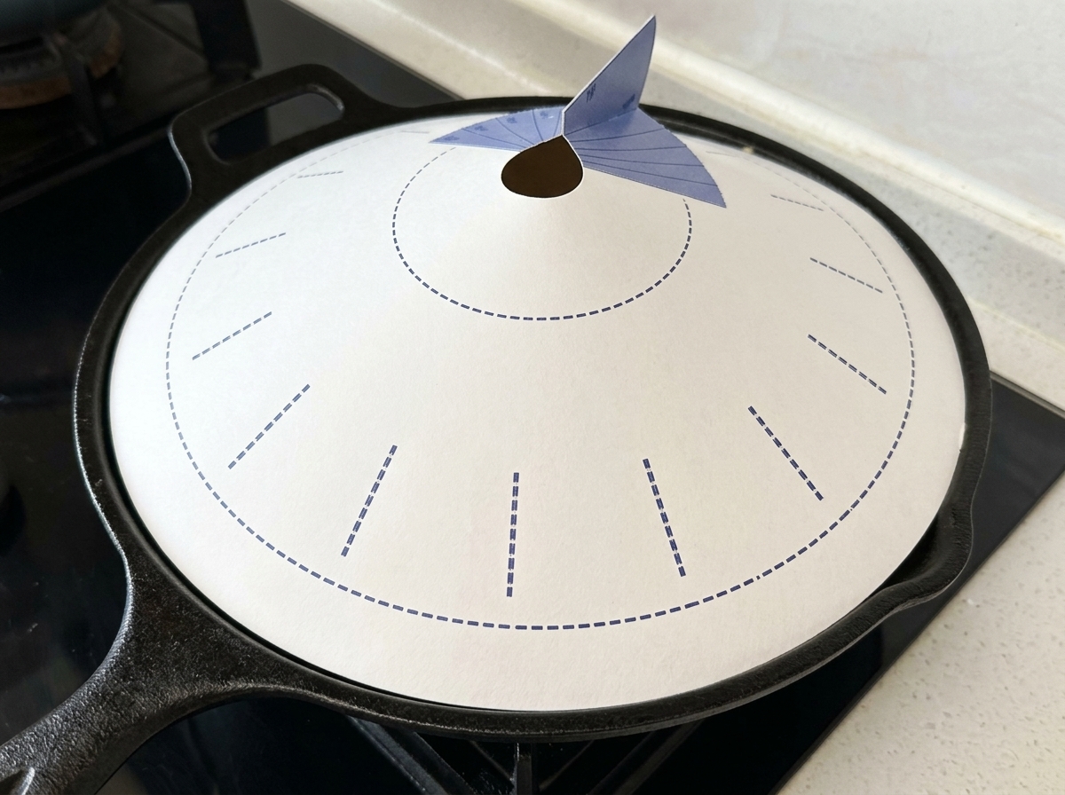 Una padella in ghisa nera coperta da un coperchio di carta conico bianco con dettagli blu, posizionata sul fornello.