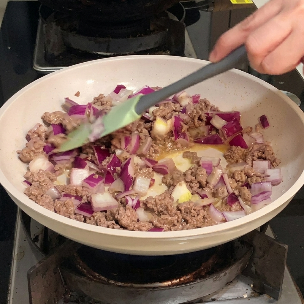 Cipolla rossa a dadini mescolata con carne di manzo macinata rosolata in una padella.