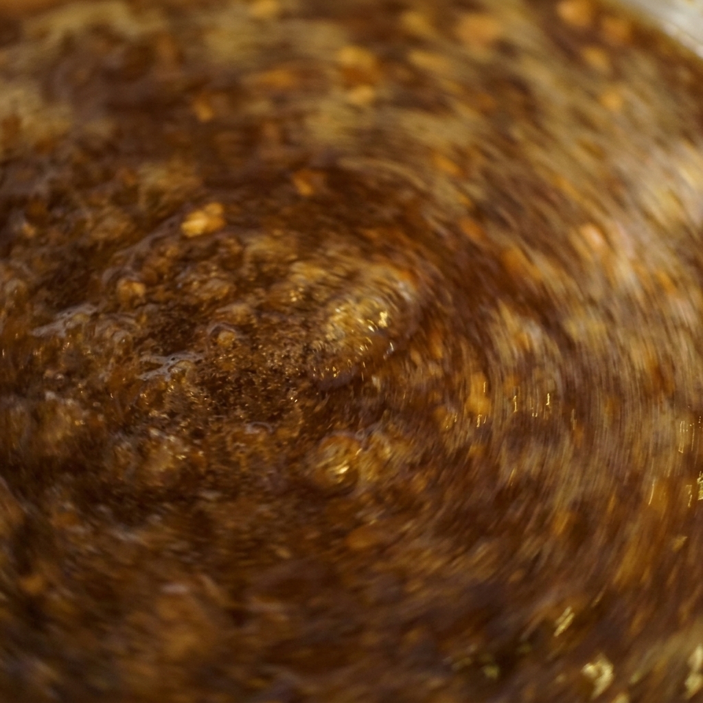 Inquadratura ravvicinata di una salsa marrone scuro che bolle vigorosamente in un pentolino mentre viene mescolata rapidamente.