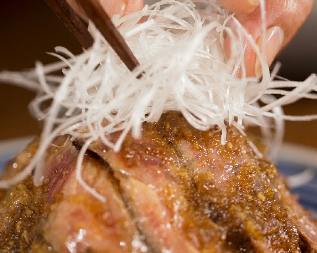 Bacchette posizionano un ciuffo di sottili filamenti bianchi di porro al centro di una ciotola di steak donburi condita.