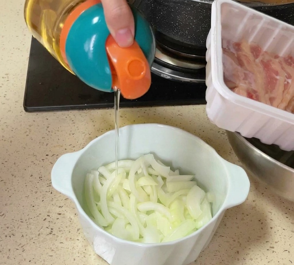 Un dispenser colorato versa olio o sale su una ciotola di cipolle crude affettate sul bancone della cucina.