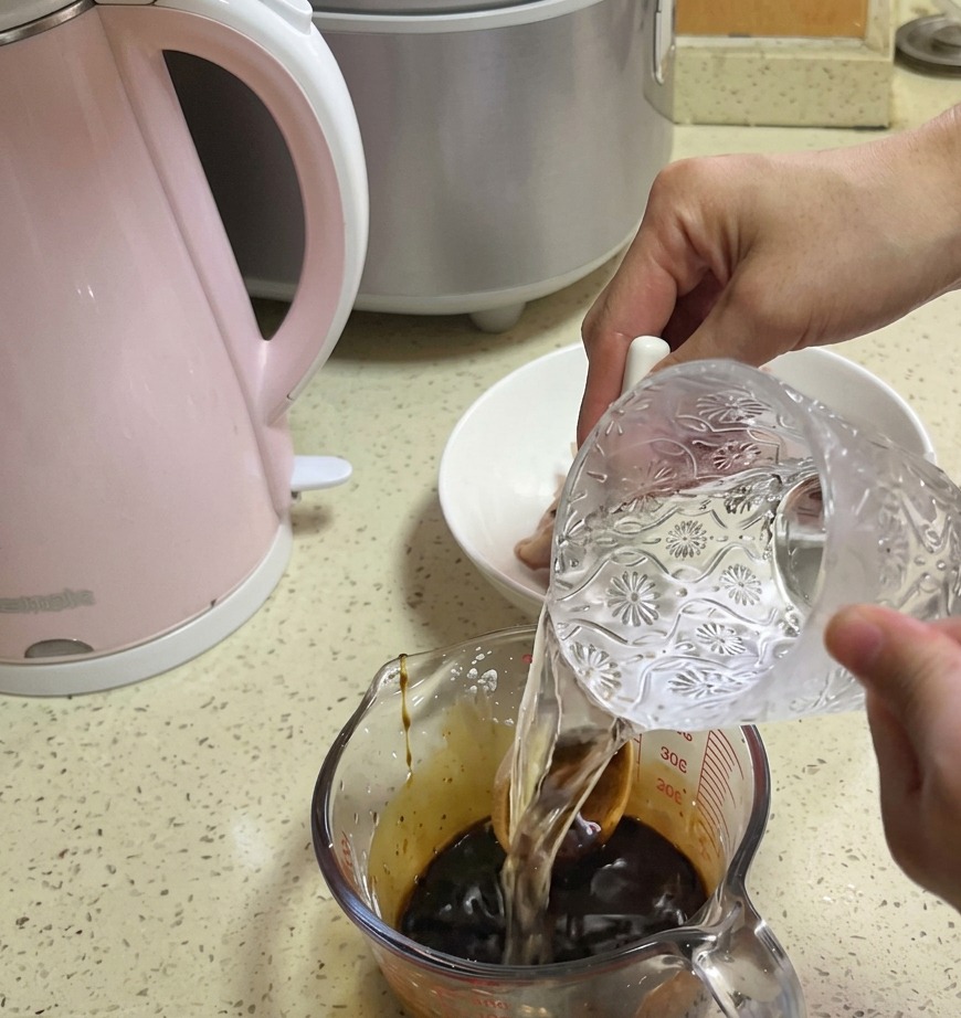 Acqua limpida viene versata da una caraffa di vetro decorata in un misurino contenente una base di salsa marrone scuro.