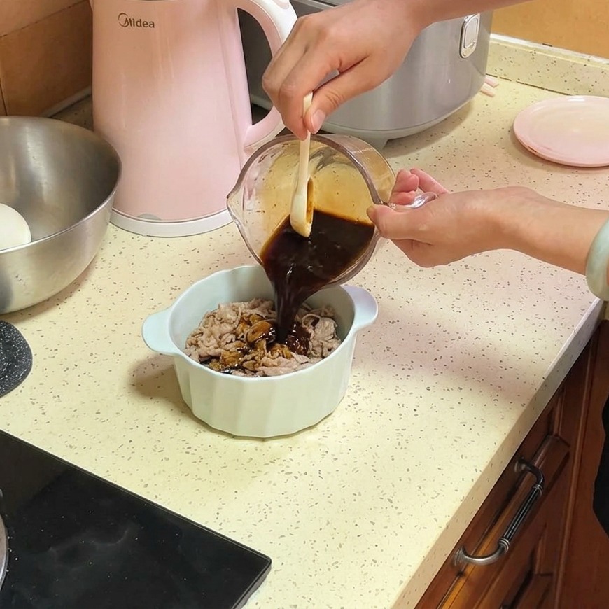 Una salsa saporita marrone scuro viene versata da un misurino di vetro su sottili fettine di manzo e cipolle in una ciotola di ceramica bianca.