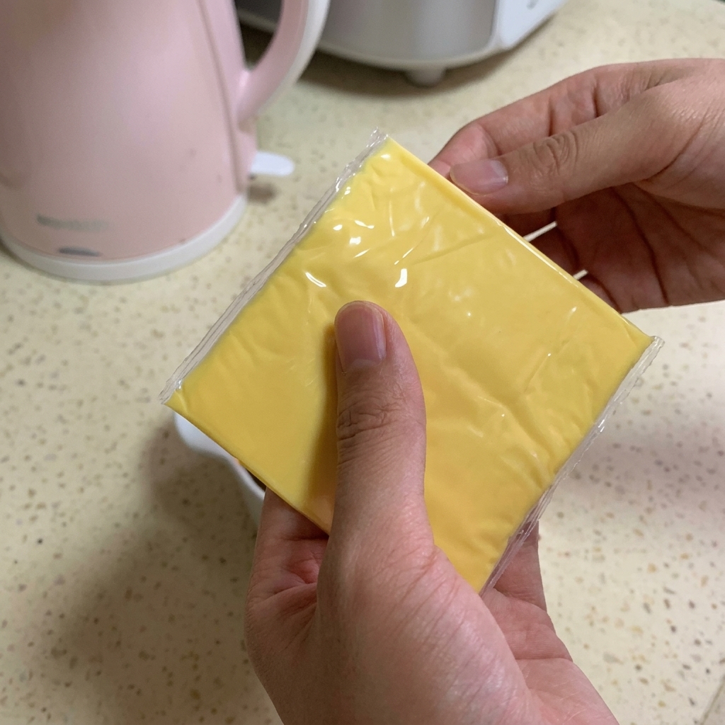 Una persona tiene due fette quadrate di formaggio fuso giallo brillante sopra una ciotola piena di manzo e salsa scura.