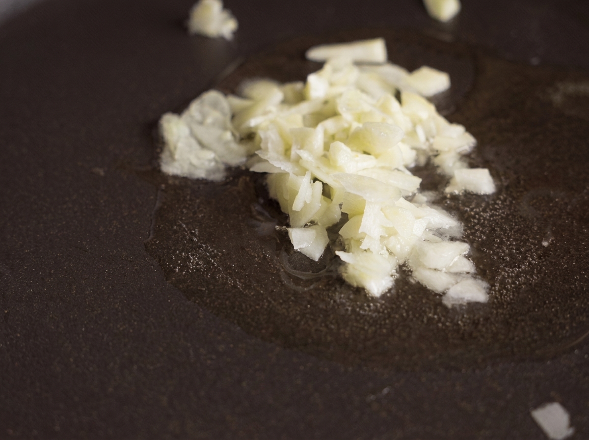 Aglio tritato finemente che soffrigge in un velo dolio trasparente in una padella antiaderente scura.
